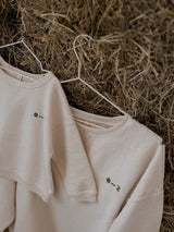 close up of women's & toddler cream sweatshirt with embroidered O~Z text hanging on straw bale wall