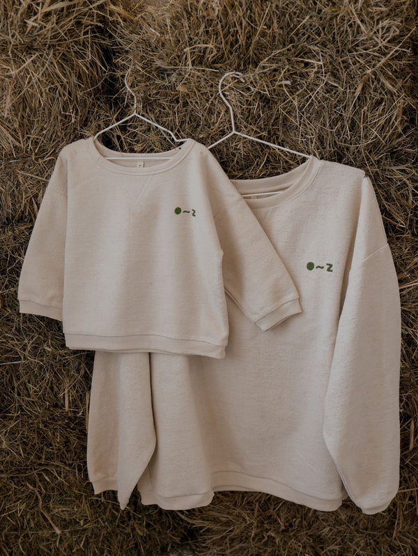 women's & toddler cream sweatshirt with embroidered O~Z text in green hanging on straw bale wall